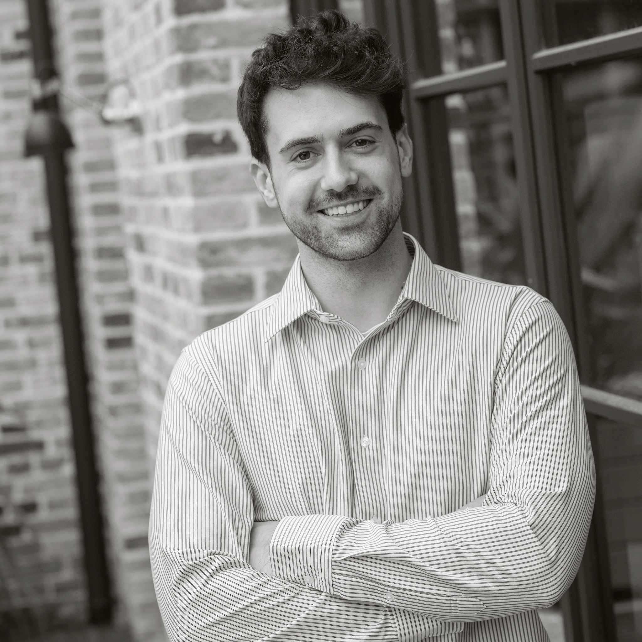 Mann im gestreiften Hemd lehnt an einer Backsteinmauer und lächelt.