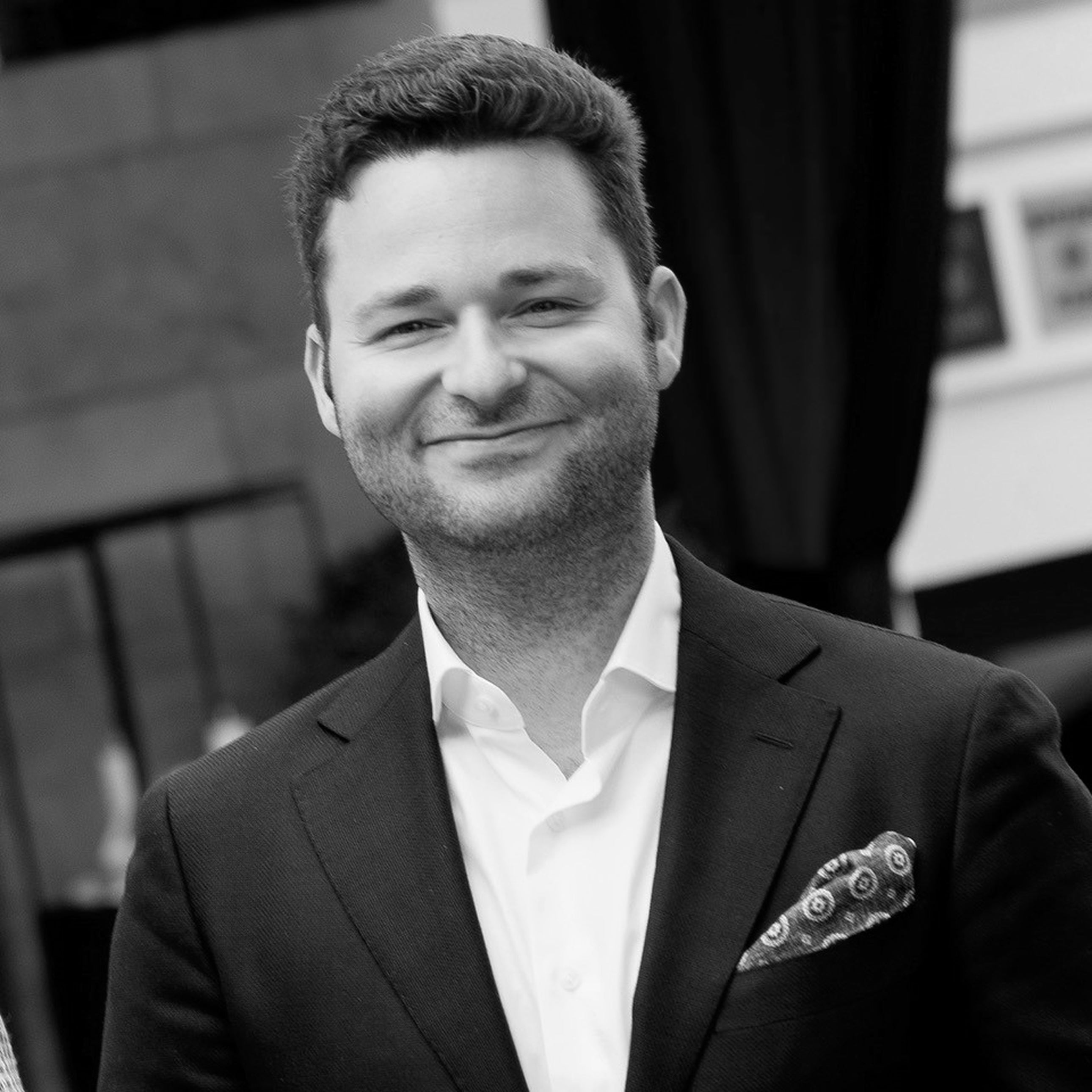 Mann trägt ein helles Hemd und dunkles Sakko und blickt direkt in die Kamera.