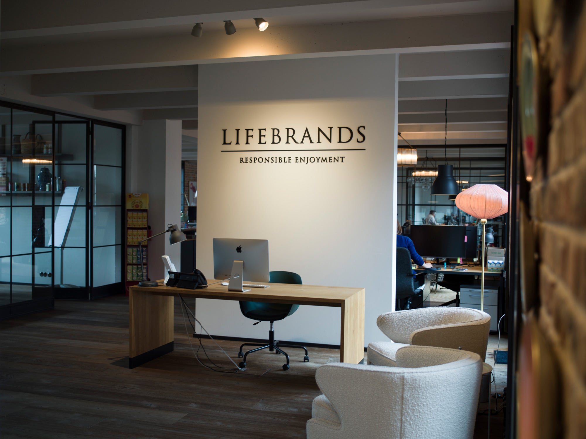 Offener Bürobereich mit Schreibtisch vor Wand, darauf steht 'Lifebrands Responsible Enjoyment'.
