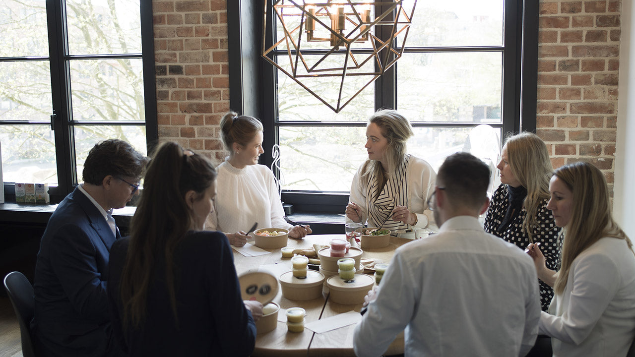 Gruppe von Menschen sitzt um einen Tisch und unterhält sich in einem Raum mit Ziegelwänden.